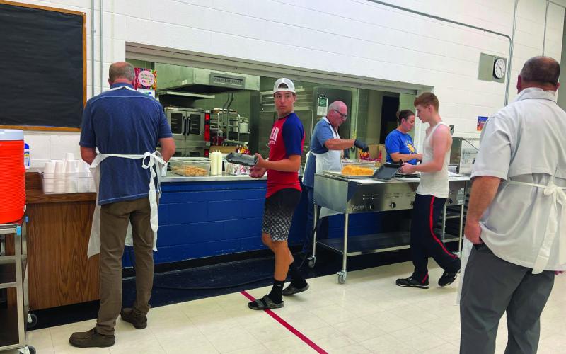 (L-R) School Board President Mark Hatloy prepares drinks as Hunter Johnson is served by Superintendent Michael Babinski while School Board Member Jessica Hermanson assists. James Larocque waits for his meal as well, while School Board Member Mike Emanuelson helps with cleanup. Photo by Kallie Christenson.