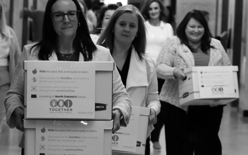 Michelle Wagner, left, carries boxes of signed petitions for a proposed ballot measure to make public school breakfasts and lunches free in North Dakota on April 9, 2026, at the Capitol. To her right is Amy Jacobson and Ashley Gaschk. All three are members of the sponsoring committee for the measure. Photo by Mary Steurer/North Dakota Monitor