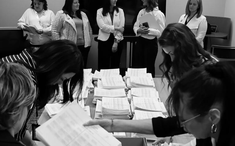 Members of the sponsoring committee for a proposed ballot measure to make public school meals free watch as staff with the North Dakota Secretary of State’s Office count petition signatures on April 9, 2026. Photo by Mary Steurer/North Dakota Monitor