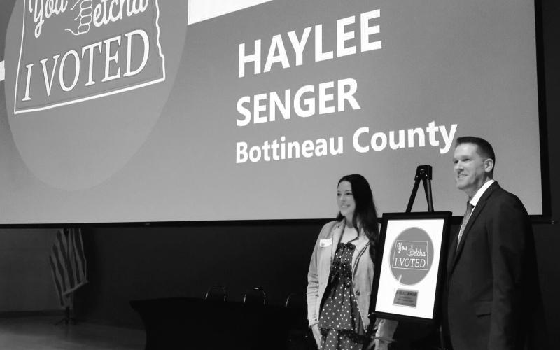 Haylee Senger, left, of Bottineau, stands next to North Dakota Secretary of State Michael Howe and her winning “I Voted” sticker design at the Heritage Center in Bismarck on March 5, 2026. Photo by Michael Achterling/North Dakota Monitor