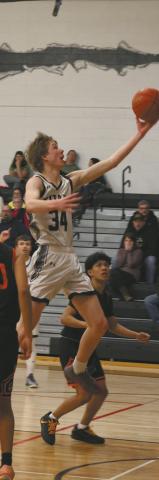 Soaring through the air, DVE senior Jack Langerud extends for the basket against Warwick Warrior defenders Feb. 20 on his home court. Photo by Jamie Rarick
