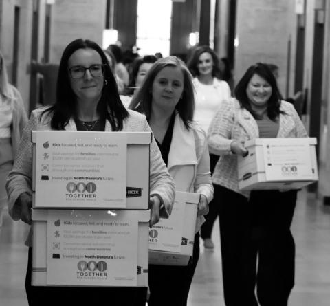 Michelle Wagner, left, carries boxes of signed petitions for a proposed ballot measure to make public school breakfasts and lunches free in North Dakota on April 9, 2026, at the Capitol. To her right is Amy Jacobson and Ashley Gaschk. All three are members of the sponsoring committee for the measure. Photo by Mary Steurer/North Dakota Monitor
