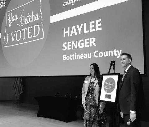 Haylee Senger, left, of Bottineau, stands next to North Dakota Secretary of State Michael Howe and her winning “I Voted” sticker design at the Heritage Center in Bismarck on March 5, 2026. Photo by Michael Achterling/North Dakota Monitor