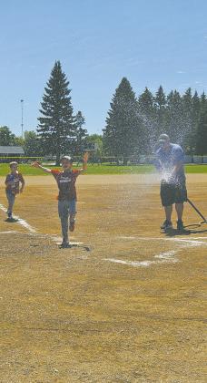 Drayton Fire Chief Jordan Grundstrom watered the field and helped the players, including Kai and Coen Delohery, cool off from high temperatures during the weekend's 10U baseball tournament. Photo by Jamie Rarick