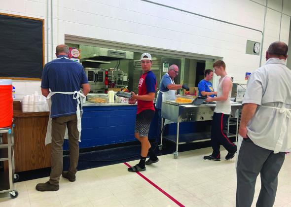 (L-R) School Board President Mark Hatloy prepares drinks as Hunter Johnson is served by Superintendent Michael Babinski while School Board Member Jessica Hermanson assists. James Larocque waits for his meal as well, while School Board Member Mike Emanuelson helps with cleanup. Photo by Kallie Christenson.
