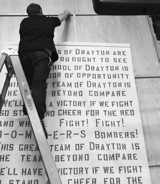 Drayton Public School custodian Matt Vold is pictured hanging the banner in its temporary location before graduation. Photo by Lyle Van Camp.