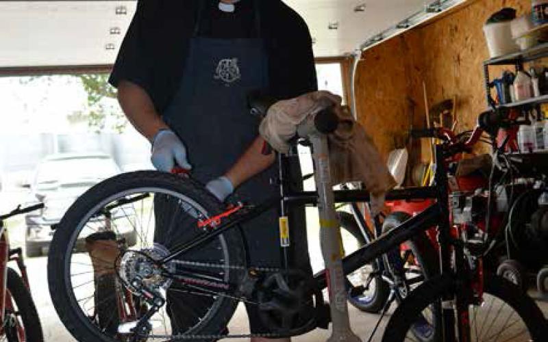 Rev. Lefor tunes up one of the eight bikes to be given away as door prizes at the Nepomuk Narly cycling race to be held June 22 in Pisek. Photo by Todd Morgan, Walsh County Record.