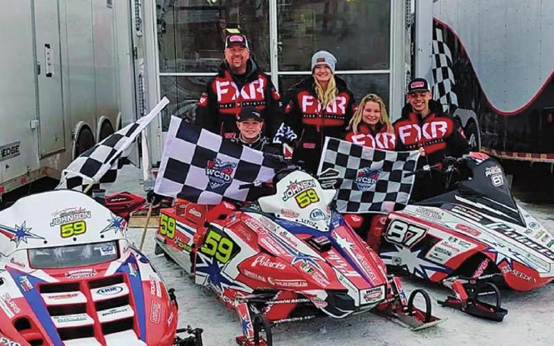 Hunter Johnson pictured with his three championship flags and the Johnson Racing sleds. Pictured left to right Hunter Johnson, Scott Johnson (back), Amber Johnson, Madison Phillips, and Jaden Haagenson Photo submitted by Johnson Racing