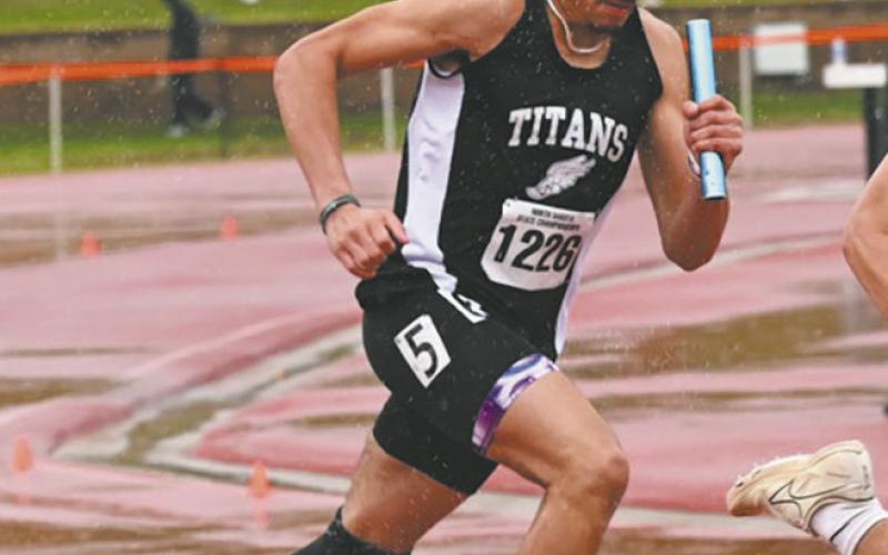 Mason Pollestad grips the baton as he navigates slippery track conditions during the relay. Photo by Ashley Schafer