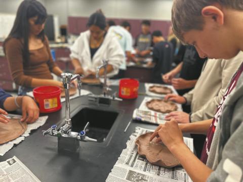 North Valley CTE students Julissa Garcia (left), Daphneiris Almonte, and Aaron Linner press prairie plants into clay plates as part of the Thinking Like a Prairie workshops. Plates will be fired and glazed and used at a potluck as part of the program next Spring. Photo Josh Anderson.
