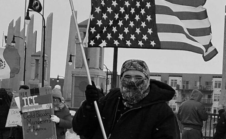 Jerrod Baetsch of West Fargo, North Dakota, stands with an American flag upside down, a sign of distress, on the Veterans Memorial Bridge over the Red River in Fargo on Jan. 10, 2026. Photo by Jeff Beach/North Dakota Monitor