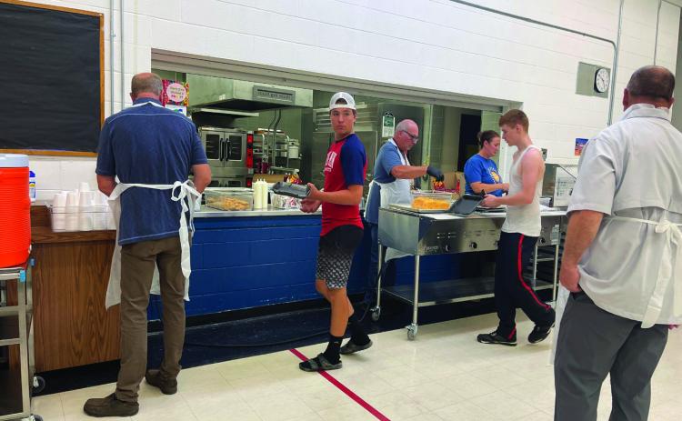 (L-R) School Board President Mark Hatloy prepares drinks as Hunter Johnson is served by Superintendent Michael Babinski while School Board Member Jessica Hermanson assists. James Larocque waits for his meal as well, while School Board Member Mike Emanuelson helps with cleanup. Photo by Kallie Christenson.