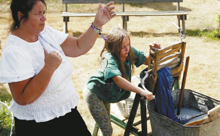 Catherine Betchel (Kari Helgoe) shares about her family while a visitor uses a wringer washer. Photo by Larry Stokke