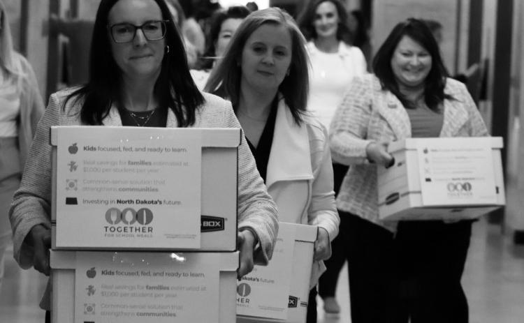 Michelle Wagner, left, carries boxes of signed petitions for a proposed ballot measure to make public school breakfasts and lunches free in North Dakota on April 9, 2026, at the Capitol. To her right is Amy Jacobson and Ashley Gaschk. All three are members of the sponsoring committee for the measure. Photo by Mary Steurer/North Dakota Monitor