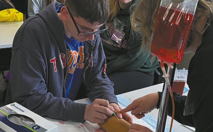 Jonah Rarick carefully inserts an IV with guidance from a hospital nurse. Submitted photo.