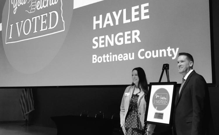 Haylee Senger, left, of Bottineau, stands next to North Dakota Secretary of State Michael Howe and her winning “I Voted” sticker design at the Heritage Center in Bismarck on March 5, 2026. Photo by Michael Achterling/North Dakota Monitor